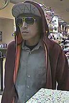 A bank robber wearing aviator-style sunglasses and having a mole above his lip who was wearing a baseball cap with the letters  on the inside bill and a burgundy-colored sweat-jacket is being sought in connection with a bank robbery.