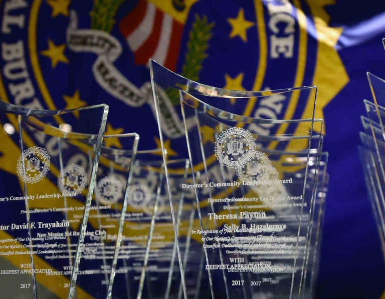 Director's Community Leadership Award trophies on table with FBI flag in the background.