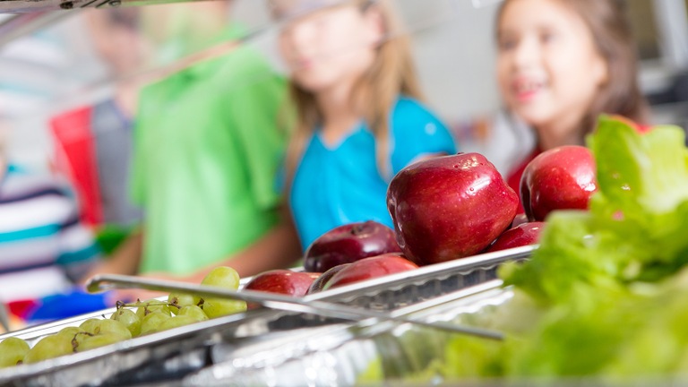 Stock image of children being served food in a cafeteria line.