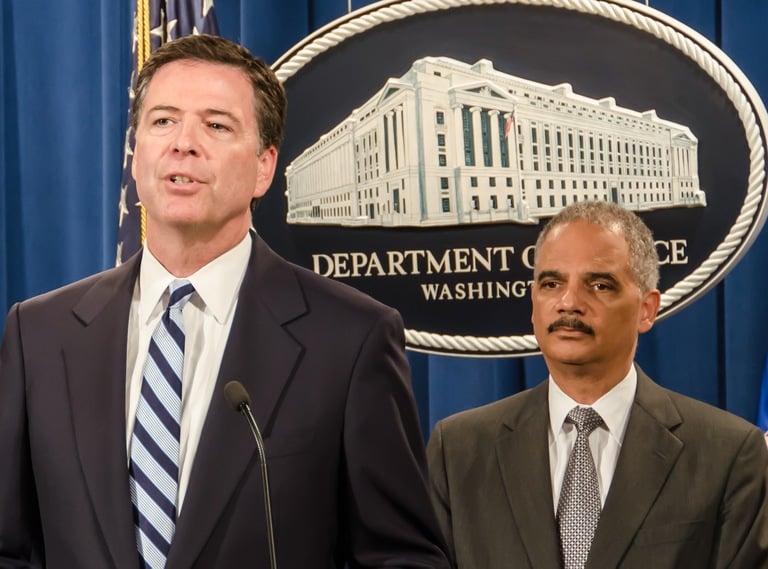 As Attorney General Eric Holder (right) looks on, FBI Director James Comey speaks at a July 2014 press conference announcing charges against BNP Paribas, which has agreed to plead guilty and pay $8.9 billion for illegally processing financial transactions on behalf countries subject to U.S. economic sanctions.