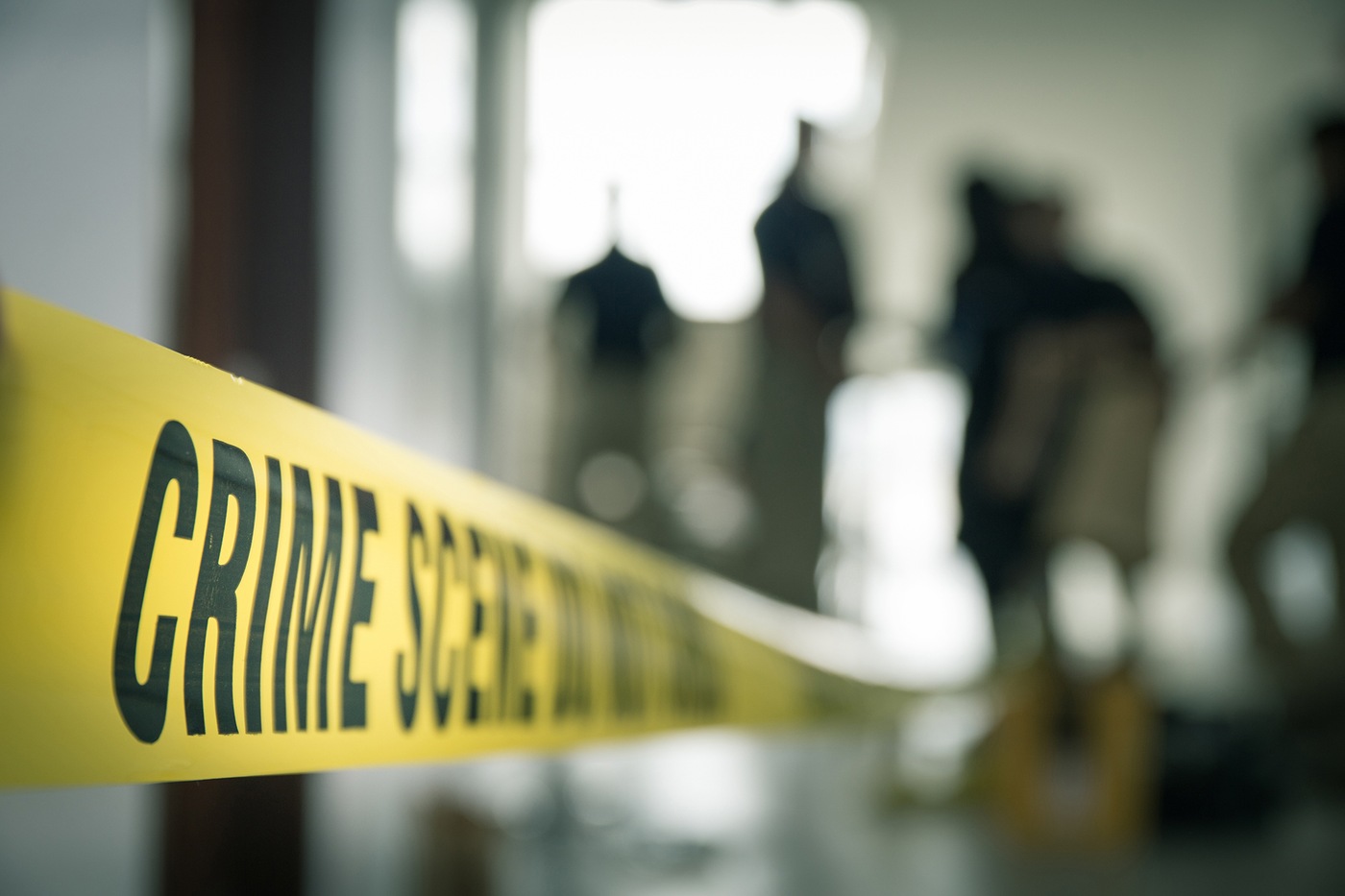 Stock image of crime scene tape with blurred crime scene investigators in the background. 
