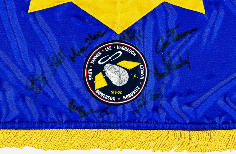 A seal from the space flight is attached to the FBI flag with autographs from each astronaut. Steveas signature is on the far left. Every space flight has its own uniquely designed seal.