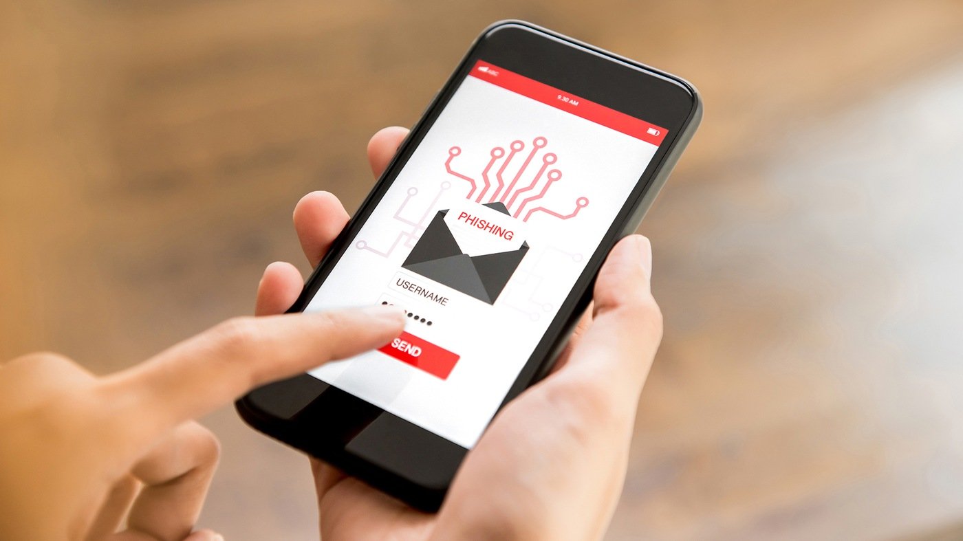 Stock image depicting a hand holding a smartphone with Phishing written on the screen and the user pushing Send. 
