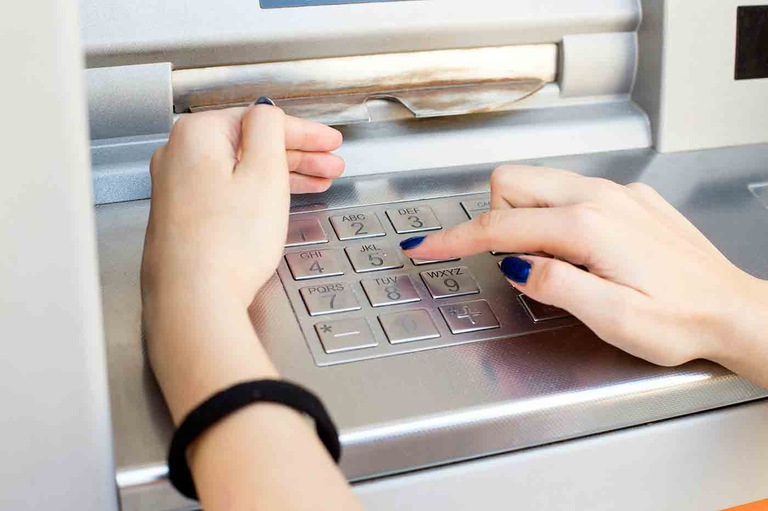 Stock image depicting a woman shielding an ATM keypad with one hand while entering a PIN with her other hand.
