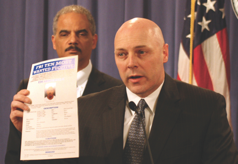 FBI Executive Assistant Director Shawn Henry, with Attorney General Eric Holder, holds up a Most Wanted poster of Barrio Azteca gang leader Eduardo Ravelo during a press conference in Washington, D.C. announcing charges against the gang in the U.S. Consulate murders last March.