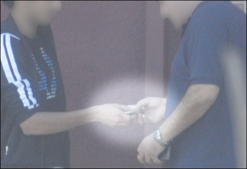 An image from surveillance video shows a DMV employee accepting cash from a license applicant.