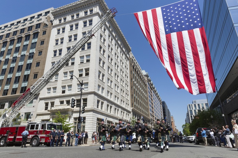 Bagpipers march beneath an American flag during the Blue Mass in Washington, D.C. on May 7, 2018, an annual gathering to remember the contributions of those who have served in law enforcement and public safety agencies and to ask for continued protection for them in the future.