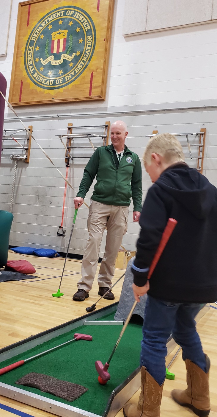 National Academy student Jesse Anderson plays mini-golf in the FBI Academy gym in Quantico, Virginia, with the child of a fallen officer during a May 14, 2019 event organized by the National Academy and the non-profit Concerns of Police Survivors (C.O.P.S).