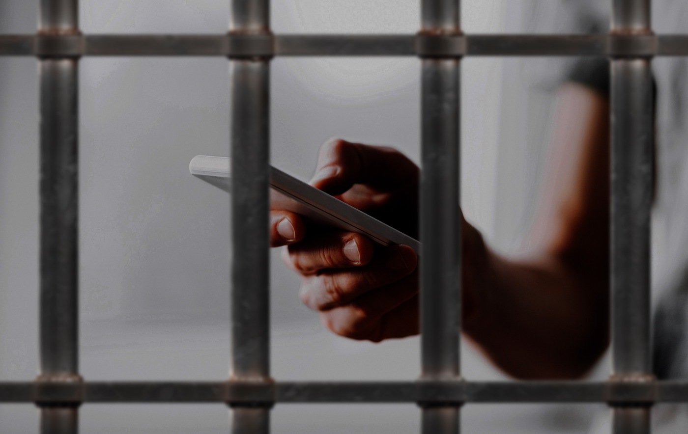 Stock image of a prisoner in a cell holding a smart phone.