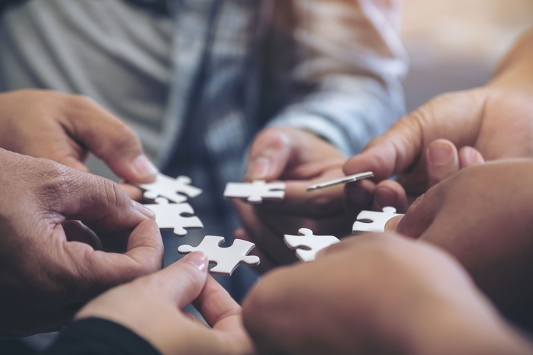 Two hands holding blank white puzzle pieces.