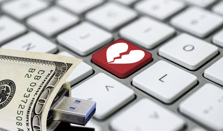 Stock graphic of computer keyboard with broken heart key and USB wrapped in money illustrating online romance scams.