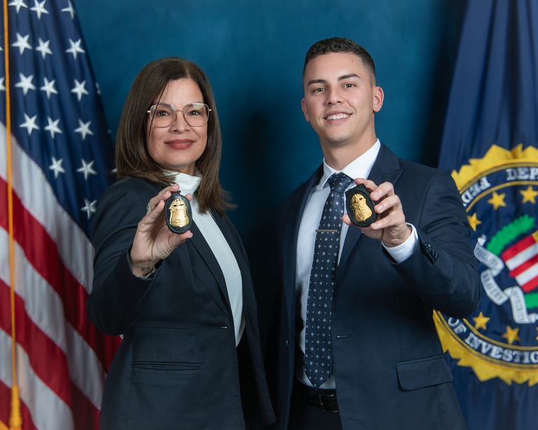 Supervisory Special Agent Marilyn Santos and Special Agent Kevin VA!zquez, both of FBI San Juan, pose for a photo with their badges in front of the American flag and the FBI flag.