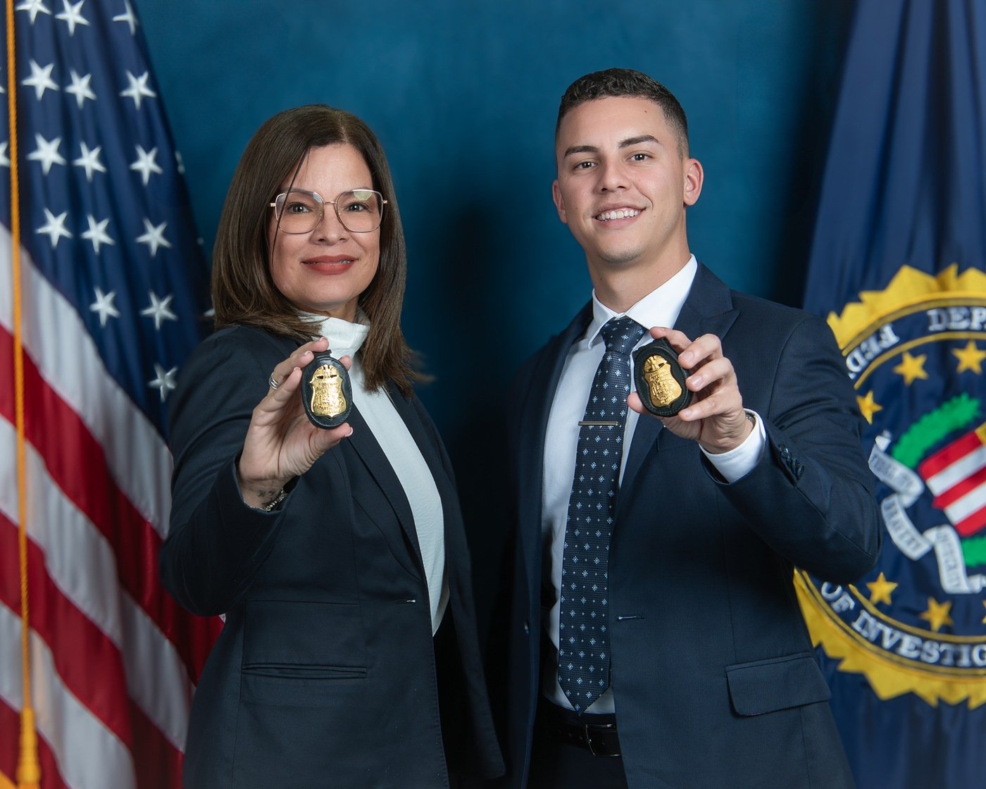 Supervisory Special Agent Marilyn Santos and Special Agent Kevin Vázquez, both of FBI San Juan, pose for a photo with their badges in front of the American flag and the FBI flag.