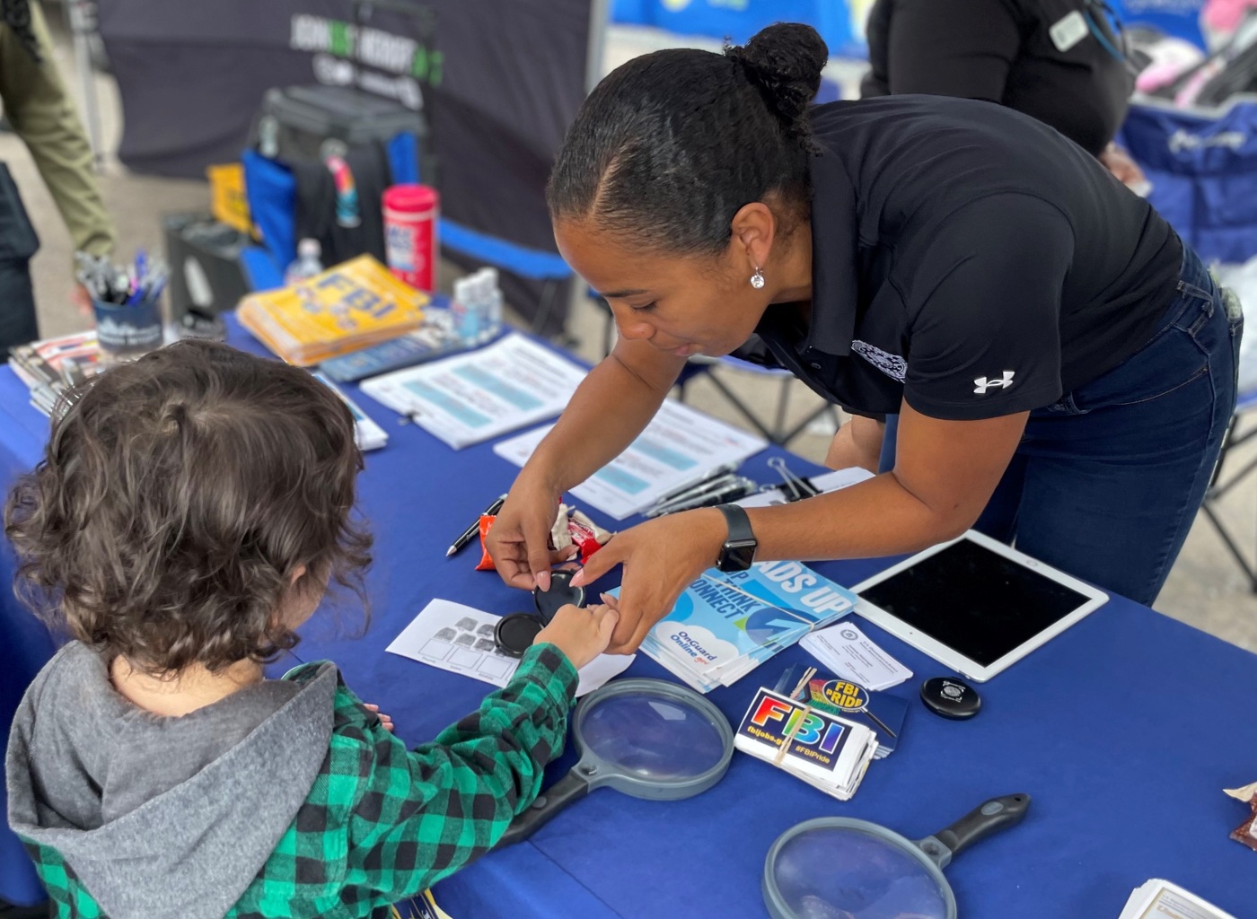 FBI San Diego employee learns over table helping a small child learn how to take fingerprints.