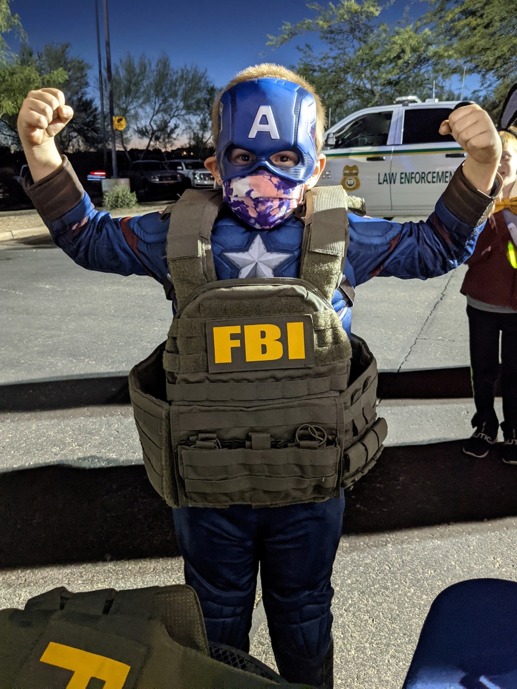 A child wearing a superhero costume and an FBI tactical vest poses for the camera during an event at the FBI Phoenix Field Office.