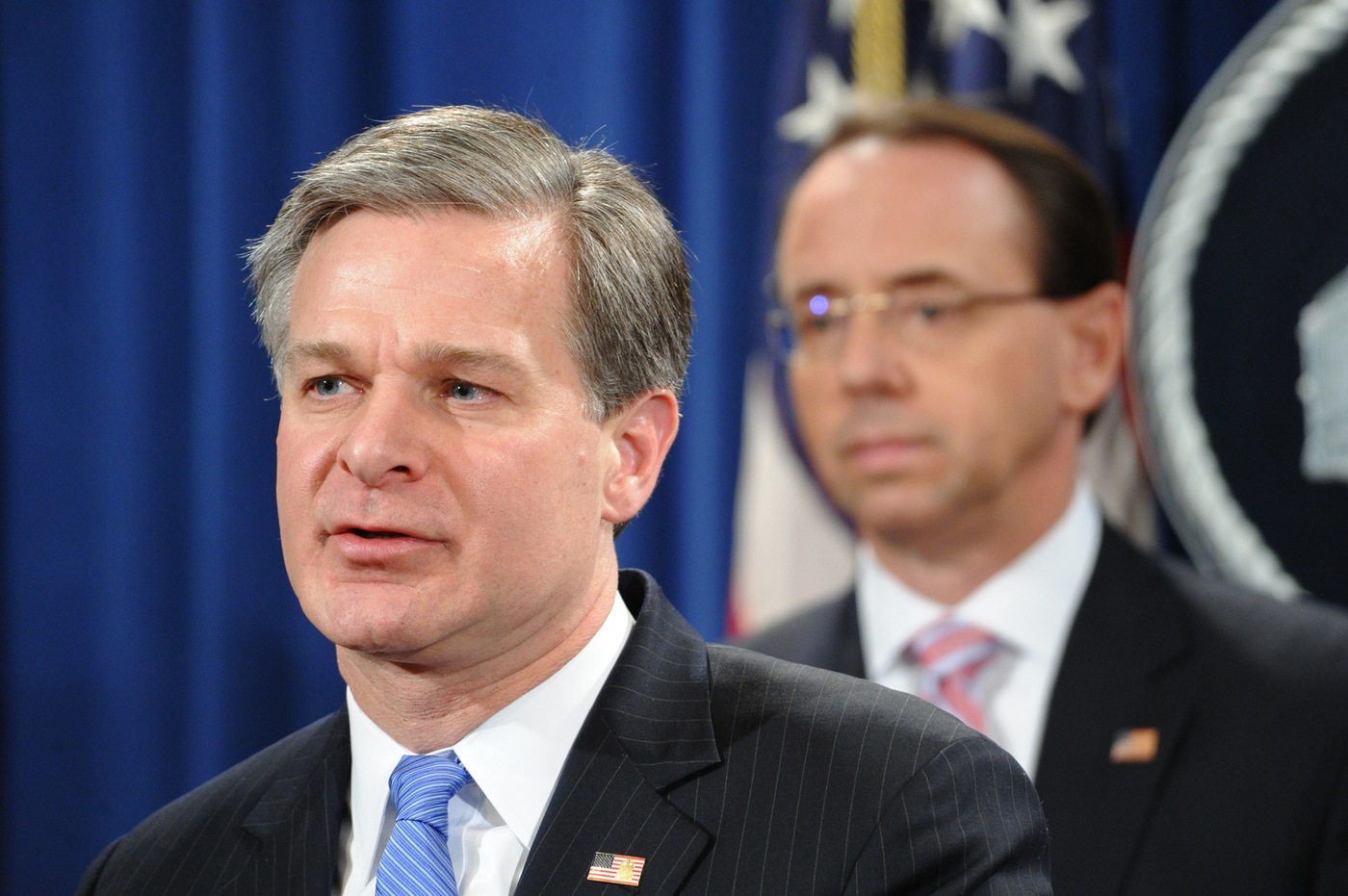 FBI Director Christopher Wray speaks at a December 20, 2018 press conference at the Department of Justice announcing charges against Zhu Hua and Zhang Shilong, both Chinese nationals and members of the APT 10 hacking group, as Deputy Attorney General Rod J. Rosenstein looks on.
